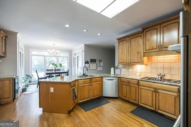 a kitchen with stainless steel appliances granite countertop wooden cabinets a sink dishwasher a stove and a refrigerator with wooden floor