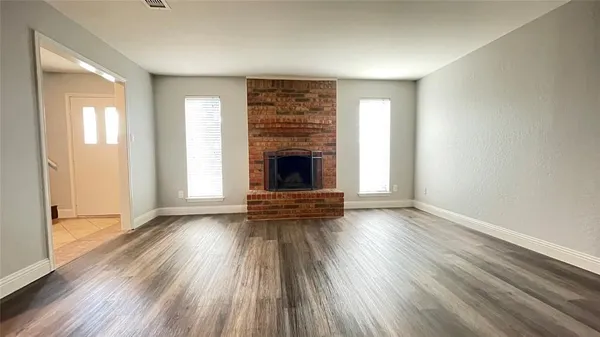 an empty room with wooden floor fireplace and windows