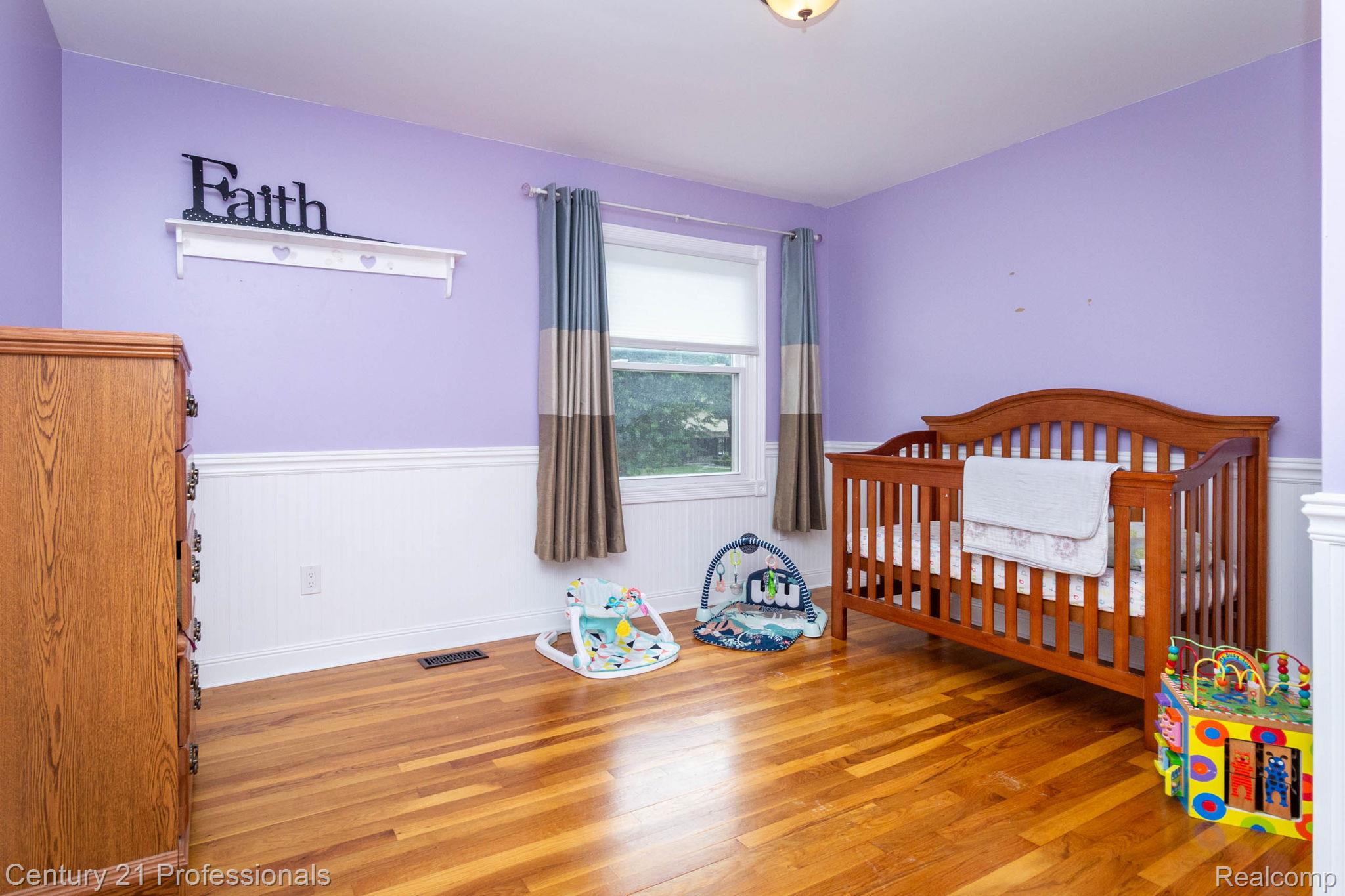 671 Bridgestone Drive Rochester, MI 48309 - Photo 33 of 50 Room featuring wood-finish flooring, a double-hung window with a roller shade, light purple walls, and white wainscoting