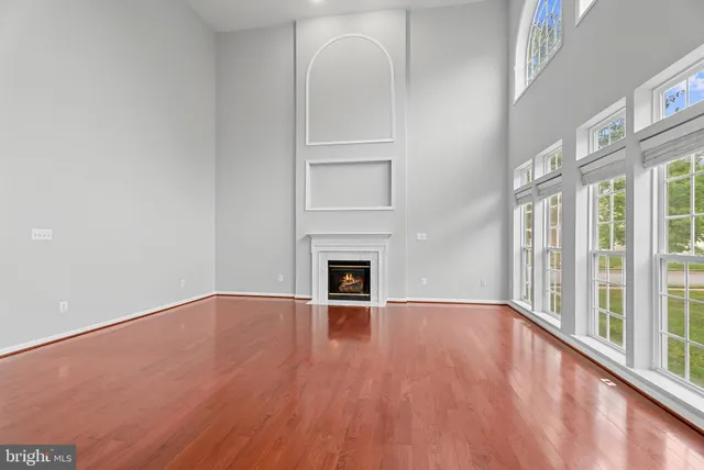 a view of an empty room with wooden floor fireplace and a window