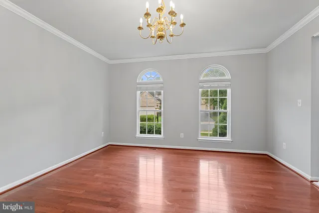 an empty room with wooden floor chandelier and windows