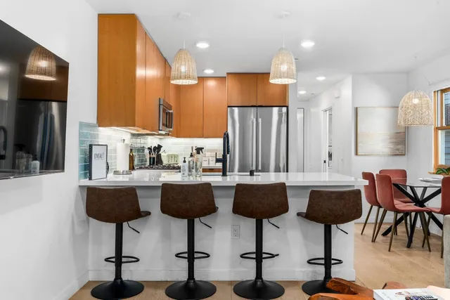 a kitchen with stainless steel appliances kitchen island a large white table chairs and a refrigerator