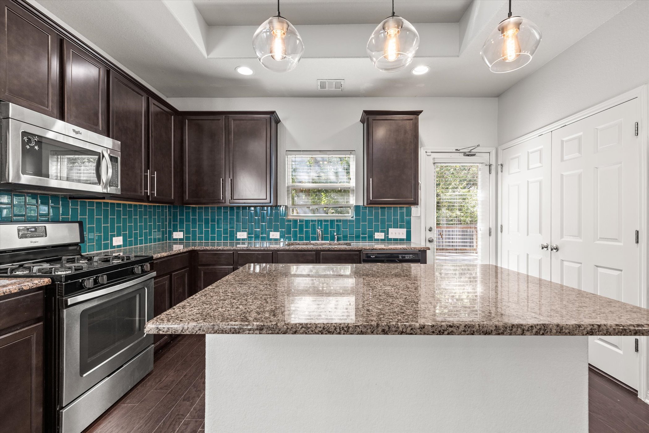 7337 Menchaca Road, Unit #22 Austin, TX 78745 - Photo 7 of 25 Kitchen featuring appliances with stainless steel finishes, cabinetry, stone countertops, backsplash, and a kitchen island. Double door to the washer and dryer closet on the right.