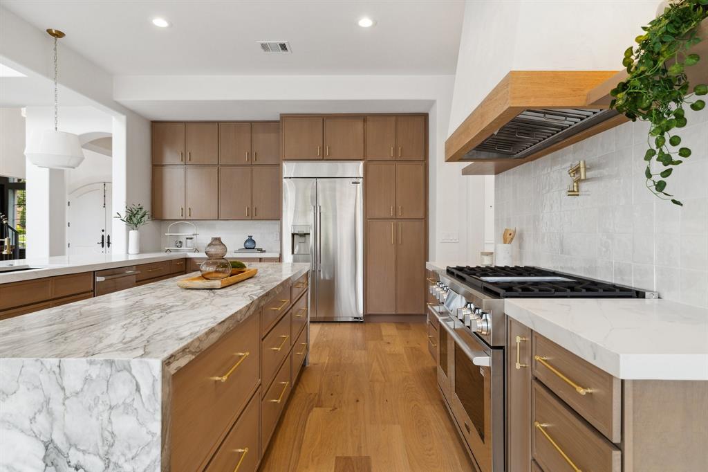 Kitchen with stainless steel appliances, wall chimney range hood, arched walkways, light wood-type flooring, and recessed lighting