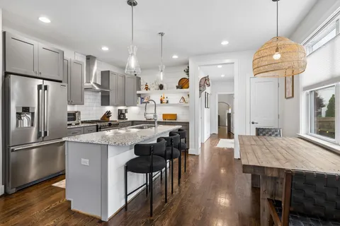 a kitchen with stainless steel appliances a dining table chairs refrigerator and wooden floor