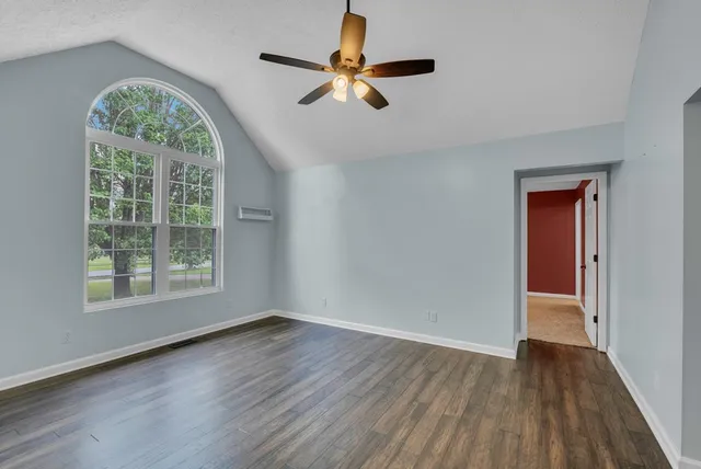 an empty room with wooden floor chandelier fan and windows