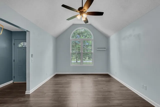 an empty room with wooden floor chandelier fan and windows