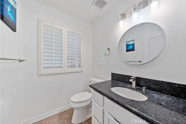 a bathroom with a granite countertop toilet a sink and a mirror