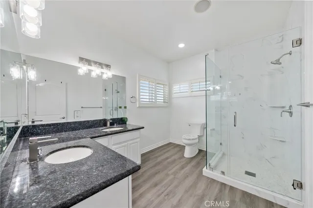 a bathroom with a granite countertop sink a toilet a mirror and shower