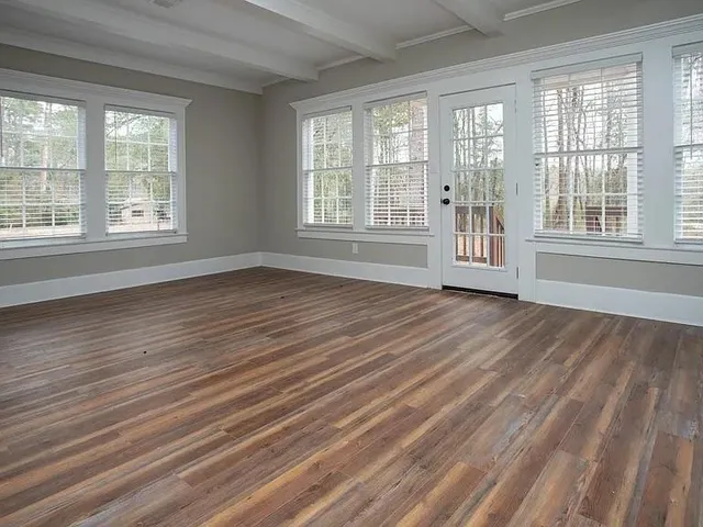 a view of an empty room with wooden floor and a window