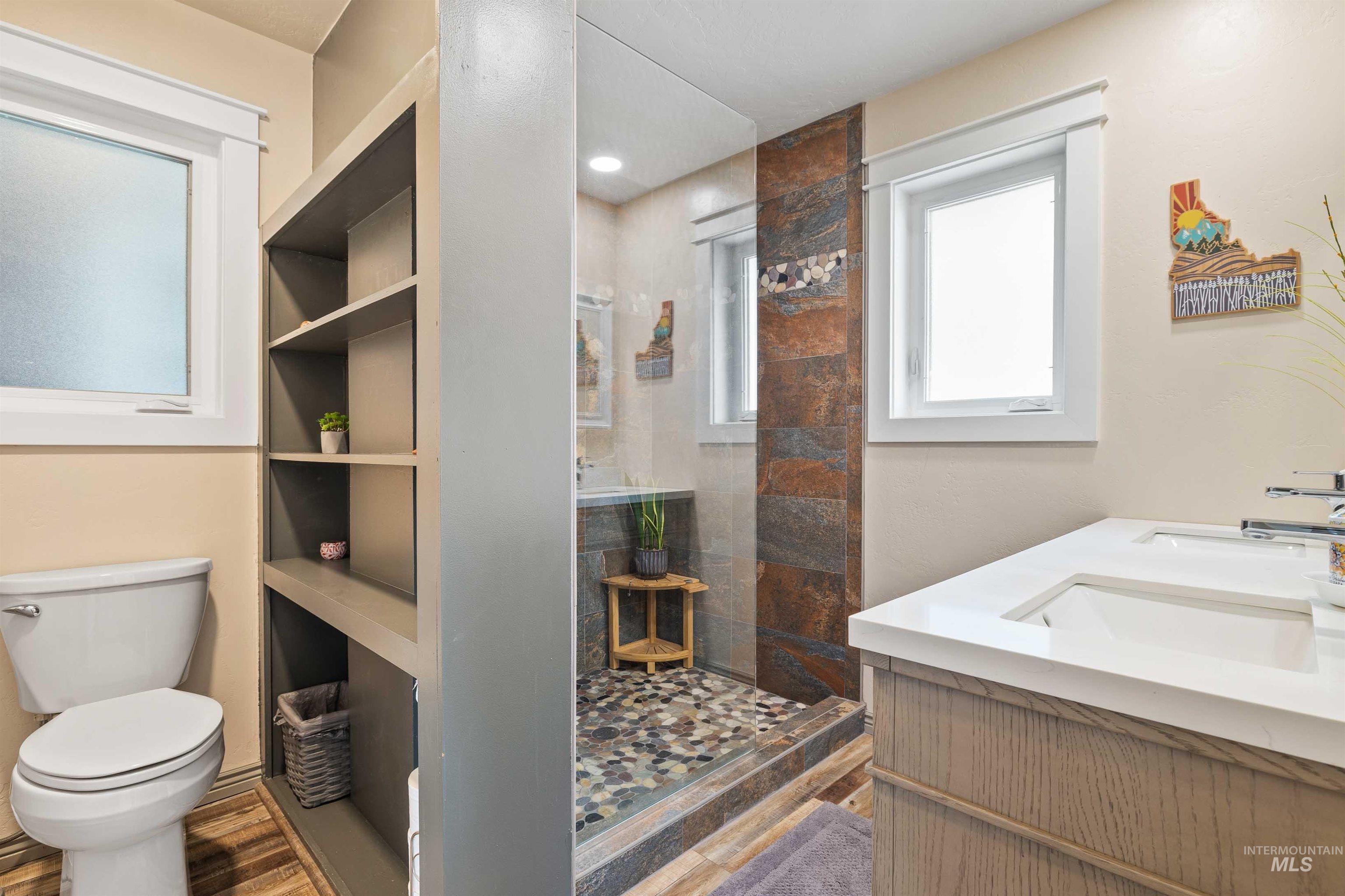 11 Bell Rapids Road Hagerman, ID 83332 - Photo 25 of 40 Modern bathroom featuring a dual vanity with undermount sinks and white countertops, a walk-in shower with stone tile accents and pebble flooring, built-in shelving, and wood-finish flooring