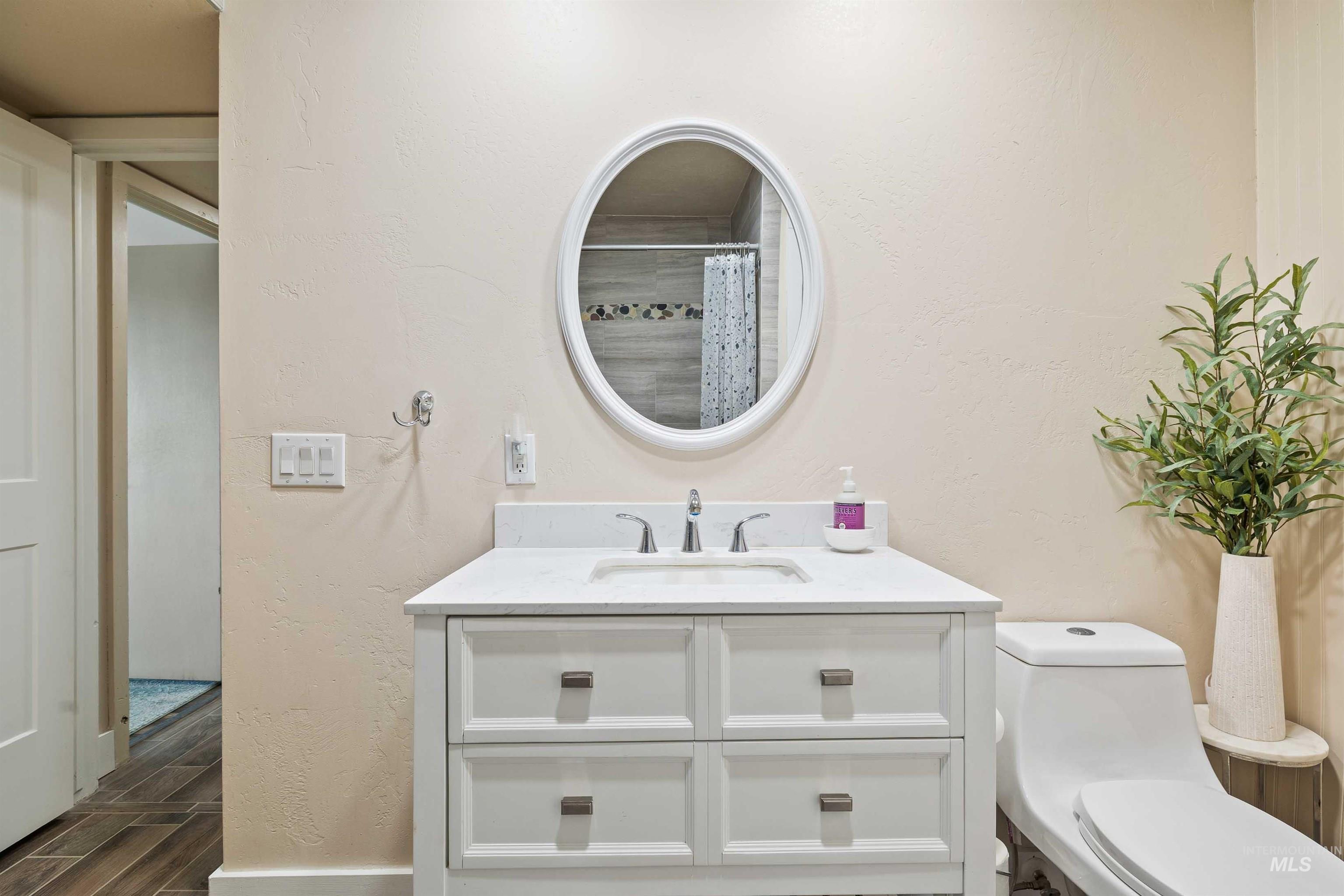 11 Bell Rapids Road Hagerman, ID 83332 - Photo 35 of 40 Bathroom featuring a white vanity with integrated sink, a white oval mirror, a modern toilet, wood-finish tile flooring, and light-colored walls
