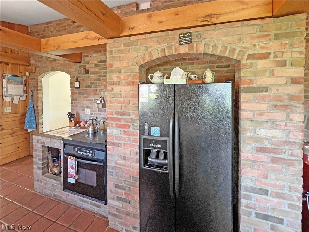 4663 East Harbor Road Port Clinton, OH 43452 - Photo 11 of 31 Kitchen with brick wall, dark tile flooring, beam ceiling, and black appliances