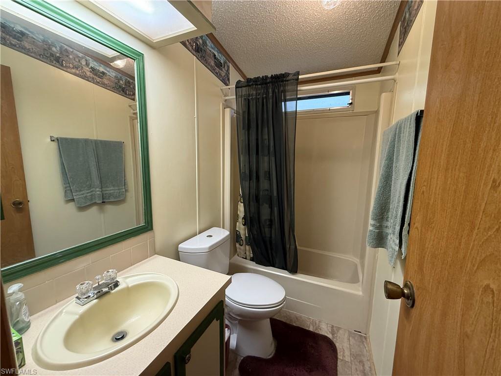 76 Atlantic Way, Unit 76 Naples, FL 34104 - Photo 15 of 18 Bathroom with a textured ceiling, shower / tub combo with curtain, vanity, and decorative backsplash