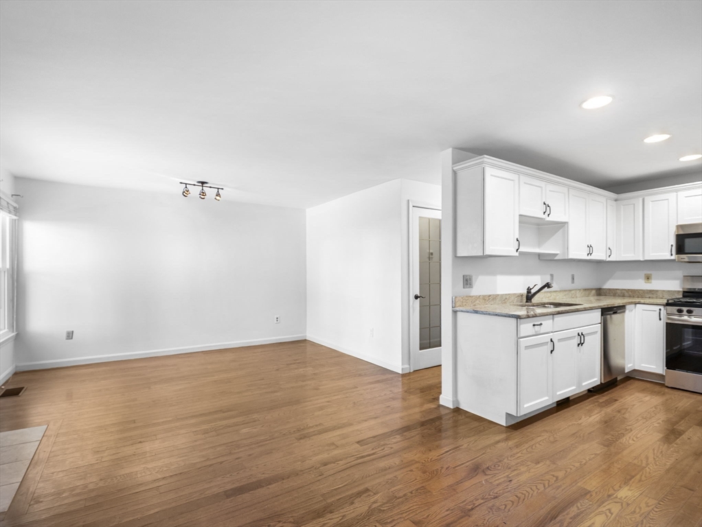 600 County Street, Unit 404 Taunton, MA 02780 - Photo 5 of 26 a kitchen with granite countertop a stove a sink and white cabinets with wooden floor
