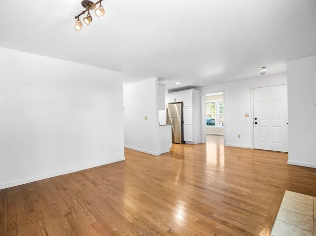 a view of an empty room with wooden floor and a kitchen