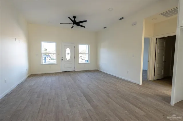 a view of empty room with wooden floor and fan