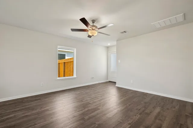 an empty room with wooden floor ceiling fan and windows