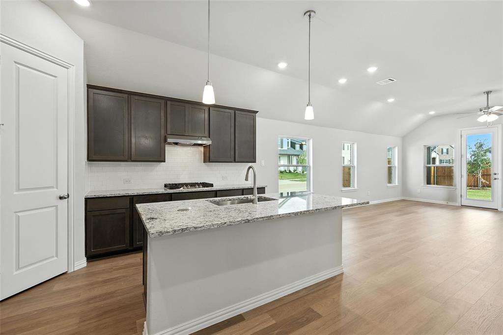 921 Alberta Spruce Road Justin, TX 76247 - Photo 2 of 24 Kitchen with vaulted ceiling, light stone counters, dark wood finish cabinets, decorative backsplash, and light wood-type flooring