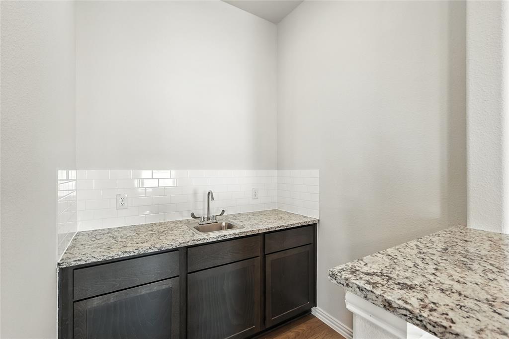 921 Alberta Spruce Road Justin, TX 76247 - Photo 10 of 24 Kitchen with light stone countertops, dark wood finish cabinetry, backsplash, and dark wood finished floors