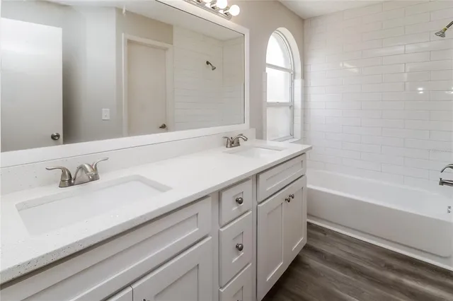 a bathroom with a granite countertop double vanity sink a mirror and a bathtub