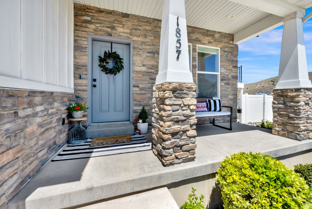 1857 Thunder Gulch Road Eagle Mountain, UT 84005 - Photo 3 of 50 Welcoming front porch featuring a stone facade, a light grey entry door, and white board-and-batten siding