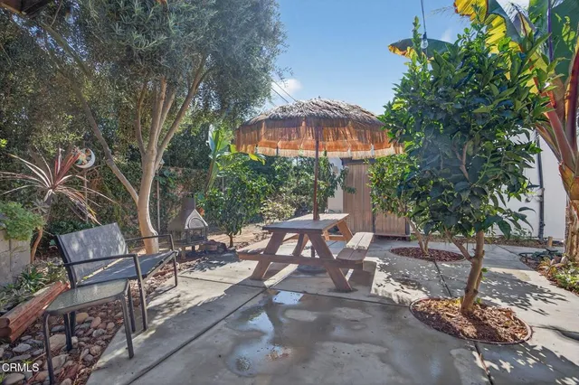a view of a patio with table and chairs under an umbrella with large trees