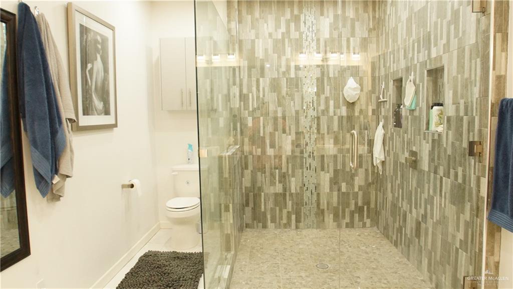 414 Ric Mar Street Edinburg, TX 78541 - Photo 24 of 36 Walk-in shower featuring glass enclosure, patterned tile walls, recessed product niches, and stone pebble flooring