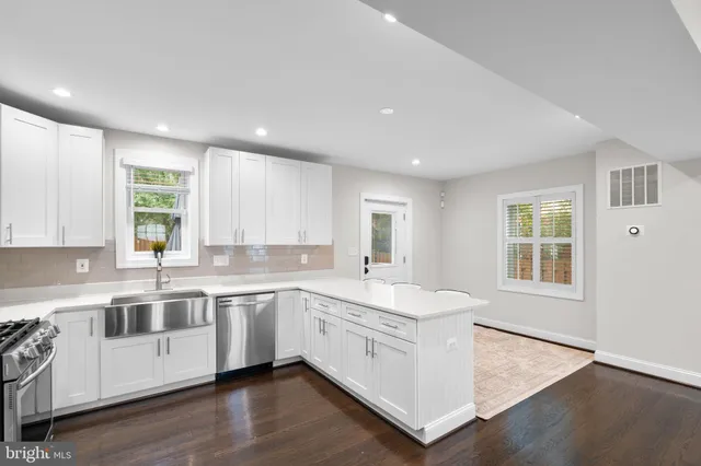 a large white kitchen with a window wooden floor and stainless steel appliances