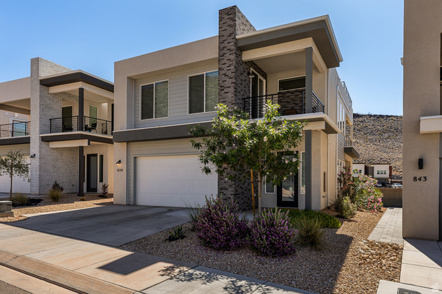 839 Walker Way St. George, UT 84770 - Photo 4 of 32 Contemporary multi-story residence featuring a two-car garage, upper-level balcony with metal railing, and a distinctive stone-clad chimney