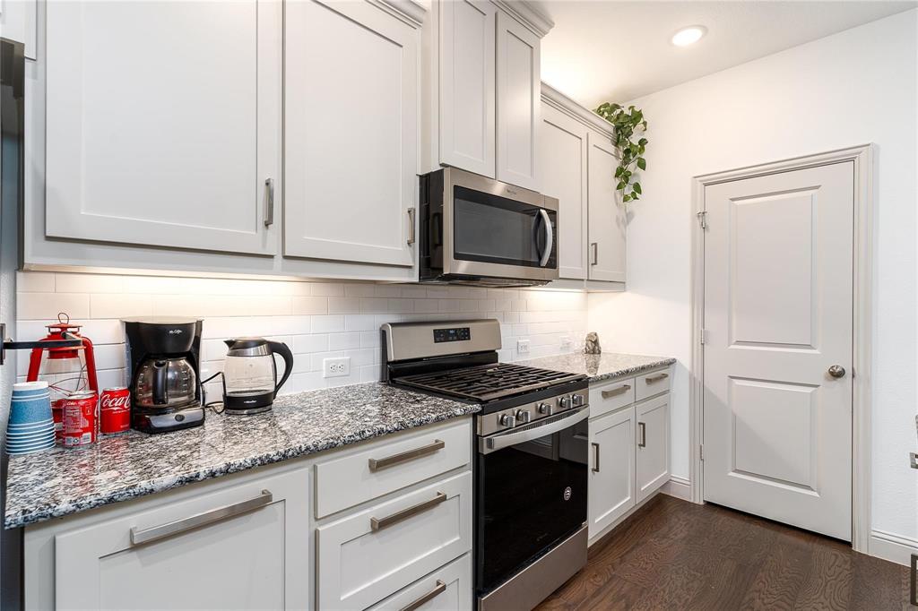 7368 Panicum Drive Frisco, TX 75033 - Photo 11 of 25 Kitchen with white cabinets, appliances with stainless steel finishes, light stone countertops, and dark wood-type flooring
