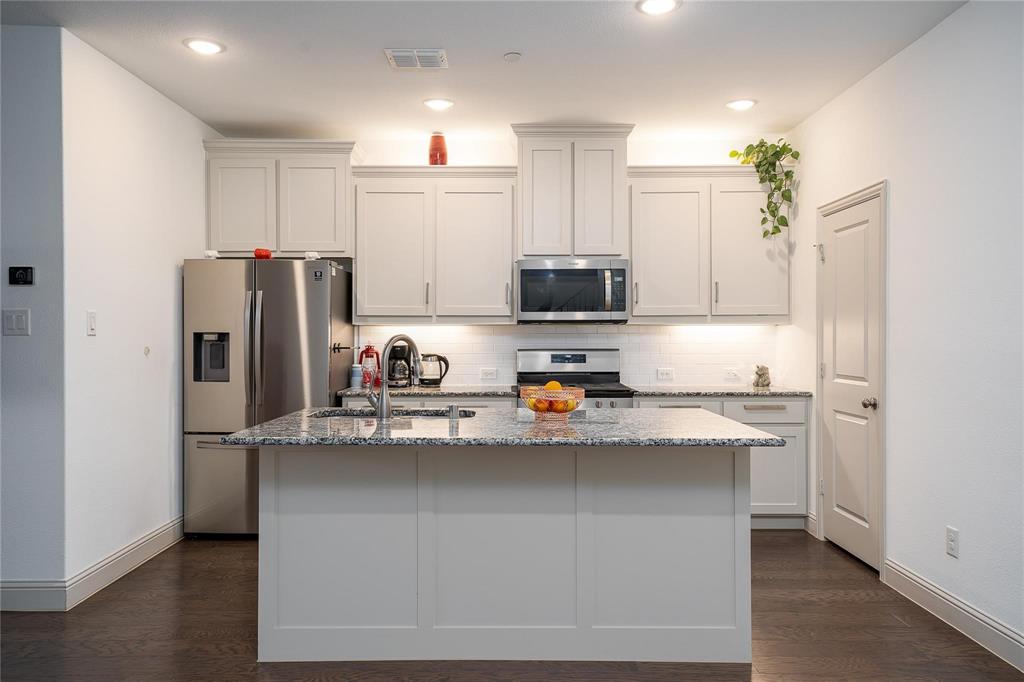 7368 Panicum Drive Frisco, TX 75033 - Photo 12 of 25 Kitchen with light stone counters, stainless steel appliances, a kitchen island with sink, sink, and white cabinetry