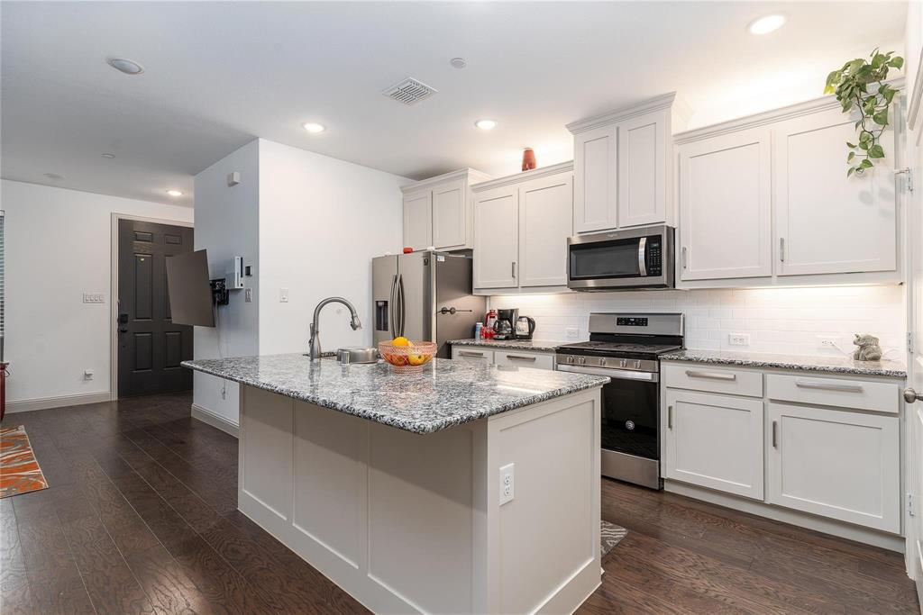 7368 Panicum Drive Frisco, TX 75033 - Photo 9 of 25 Kitchen featuring light stone counters, dark hardwood / wood-style flooring, a kitchen island with sink, white cabinets, and appliances with stainless steel finishes