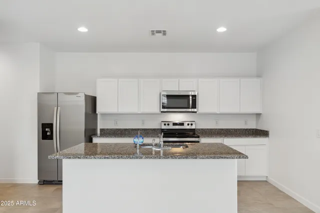 a kitchen with stainless steel appliances a sink a stove a microwave a refrigerator a stove and white cabinets