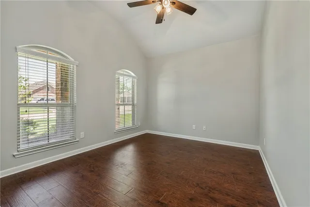 an empty room with wooden floor fan and windows