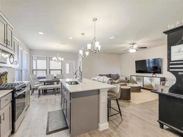 a open kitchen with stainless steel appliances kitchen island granite countertop a sink dishwasher a stove and a dining table with wooden floor