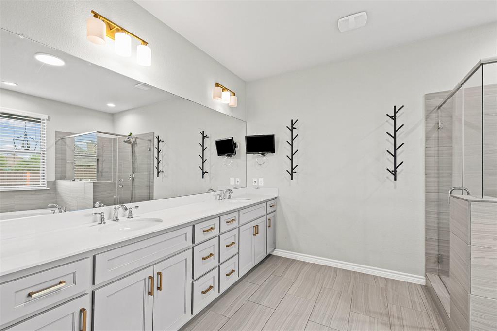 437 Prairie Run Aledo, TX 76008 - Photo 17 of 33 Spacious bathroom featuring a double vanity with white countertops, light gray cabinetry, gold-toned hardware, a frameless glass shower enclosure, and wood-finish flooring