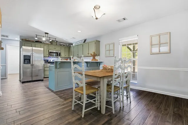 a dining room with stainless steel appliances kitchen island granite countertop a table chairs and a refrigerator