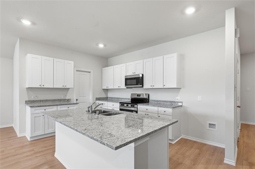 1917 Reveille Way Terrell, TX 75160 - Photo 3 of 6 Kitchen featuring a central island with an undermount sink, white cabinetry, granite countertops, stainless steel appliances, and wood-finish flooring