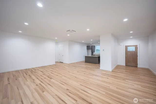 a view of an empty room with wooden floor and kitchen view