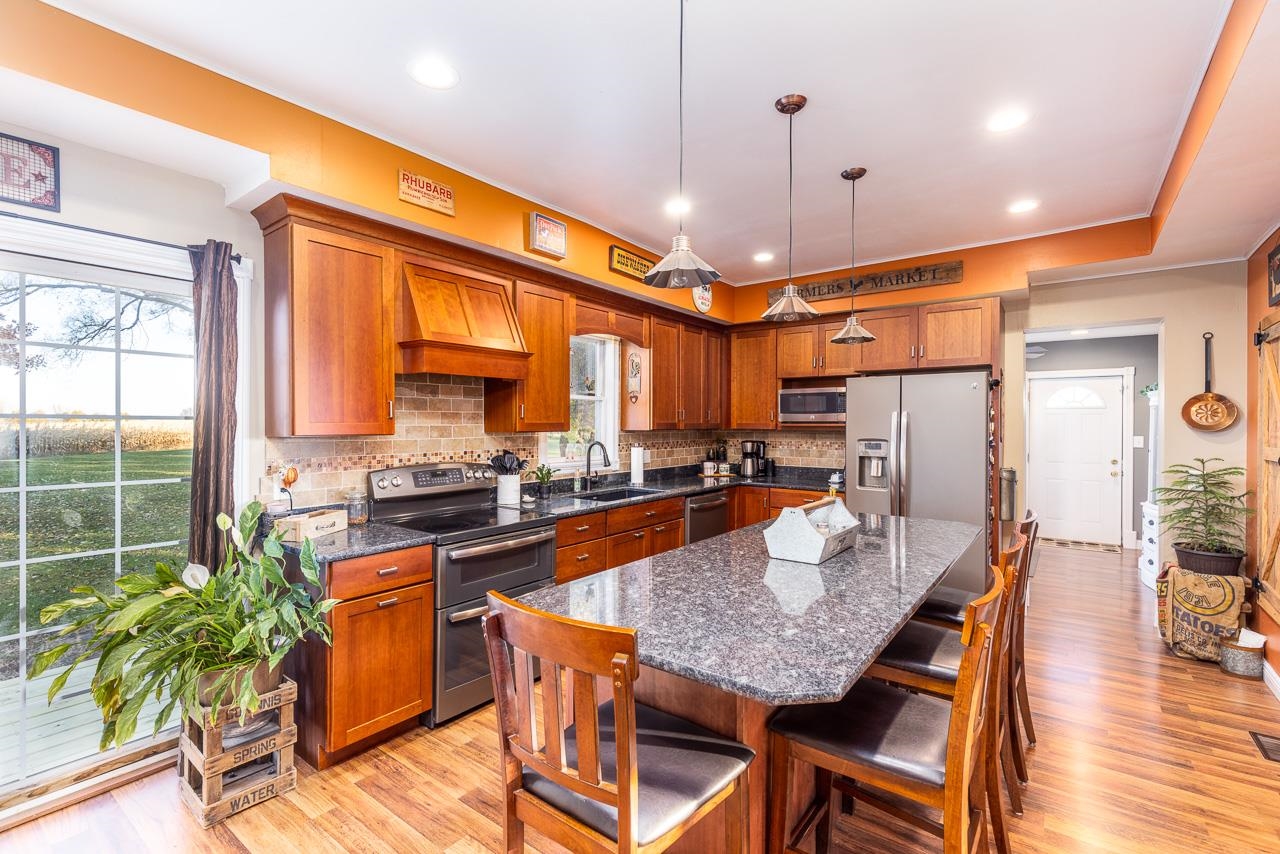 13382 Smith Road Winnebago, IL 61088 - Photo 8 of 55 a kitchen with stainless steel appliances granite countertop a stove a refrigerator a sink a dining table and chairs with wooden floor