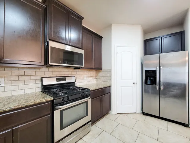 a kitchen with granite countertop stainless steel appliances a refrigerator and a stove top oven