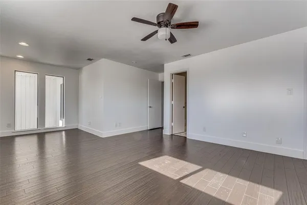 a view of an empty room with wooden floor and a ceiling fan