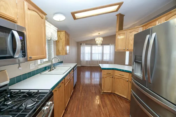 a kitchen with stainless steel appliances granite countertop a refrigerator a sink dishwasher a stove and white countertops with wooden floor