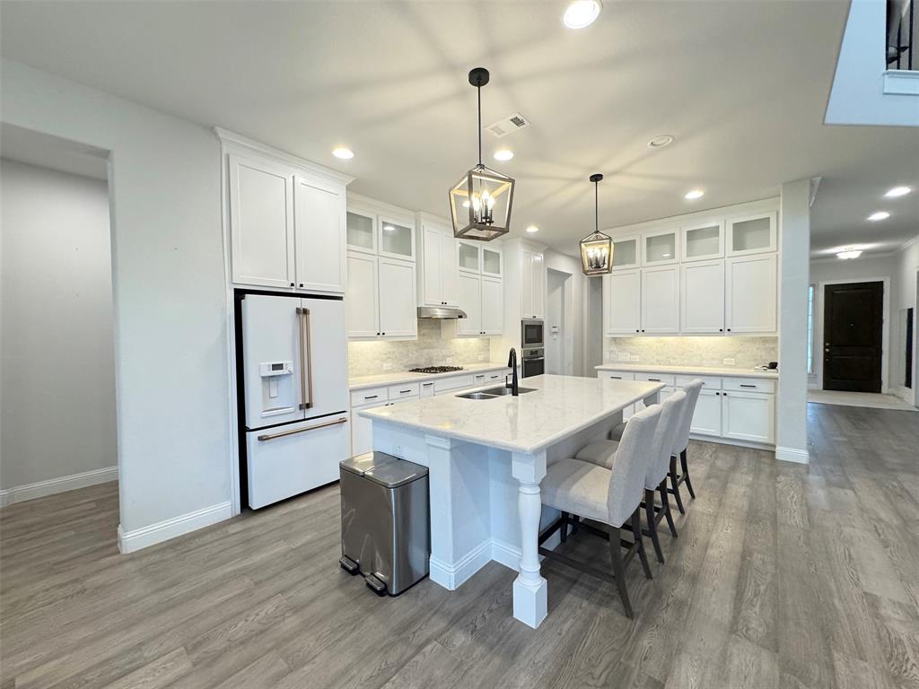 12407 Scottswood Road Frisco, TX 75035 - Photo 5 of 14 Kitchen featuring white cabinetry, high end fridge, a kitchen island with sink, and glass insert cabinets