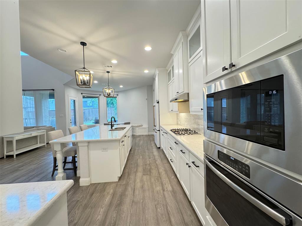 12407 Scottswood Road Frisco, TX 75035 - Photo 6 of 14 Kitchen featuring stainless steel appliances, white cabinets, a breakfast bar area, glass insert cabinets, and light stone countertops