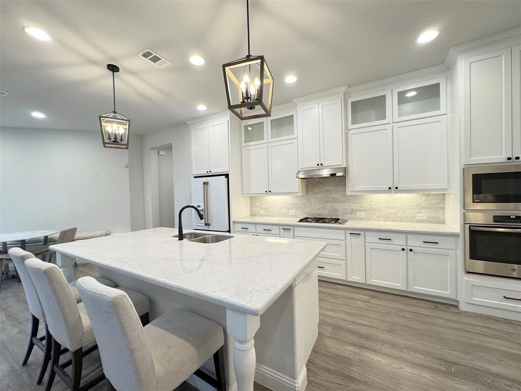 12407 Scottswood Road Frisco, TX 75035 - Photo 7 of 14 Kitchen with glass insert cabinets, white cabinetry, a kitchen bar, stainless steel appliances, and light wood-style floors