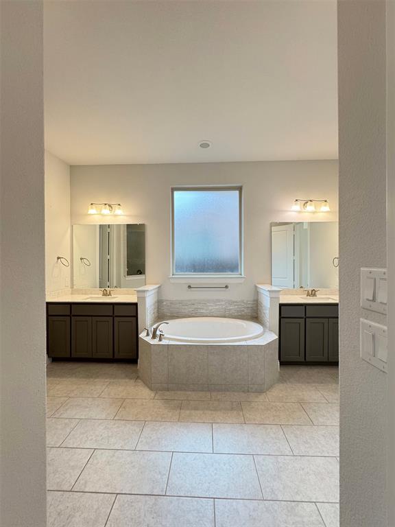12407 Scottswood Road Frisco, TX 75035 - Photo 10 of 14 Full bathroom with two vanities, a garden tub, light tile patterned floors, and a textured wall