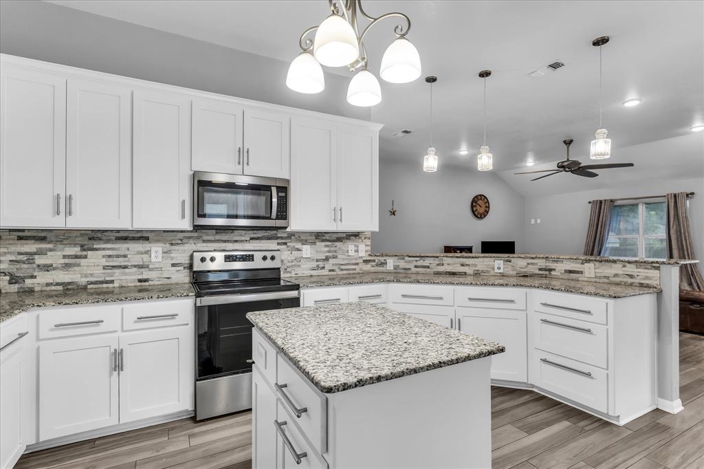 7 Market Loop Morgan's Point Resort, TX 76513 - Photo 7 of 31 Modern kitchen featuring white cabinetry, granite countertops, a textured tile backsplash, stainless steel appliances, and a central island