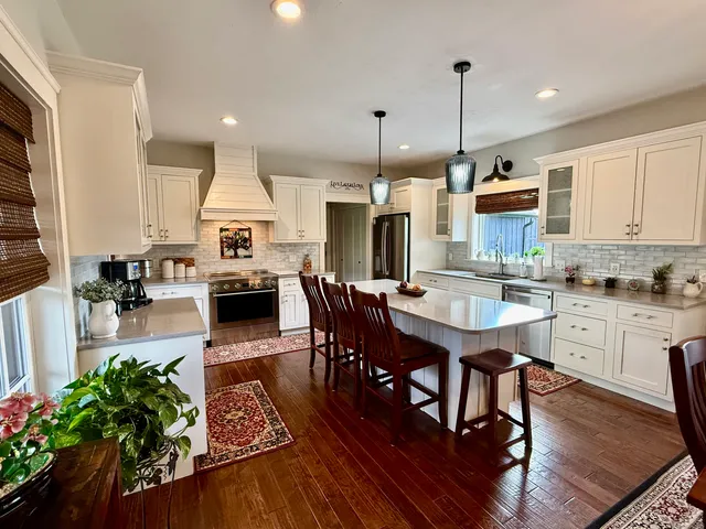 a open kitchen with stainless steel appliances granite countertop a stove a refrigerator a kitchen island a dining table and chairs with wooden floor
